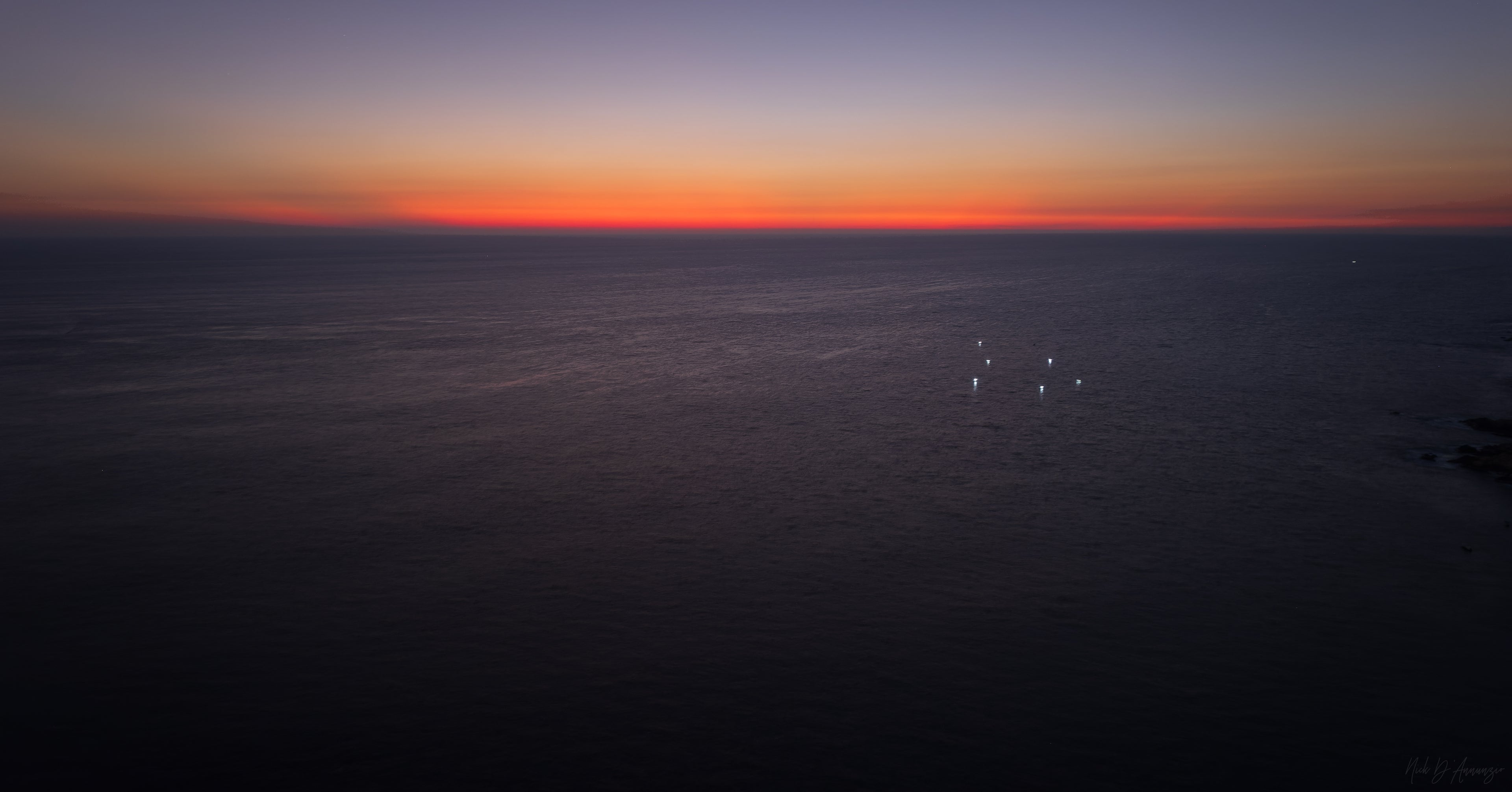 Sunset over a body of water with a dark sky transitioning from orange to blue.