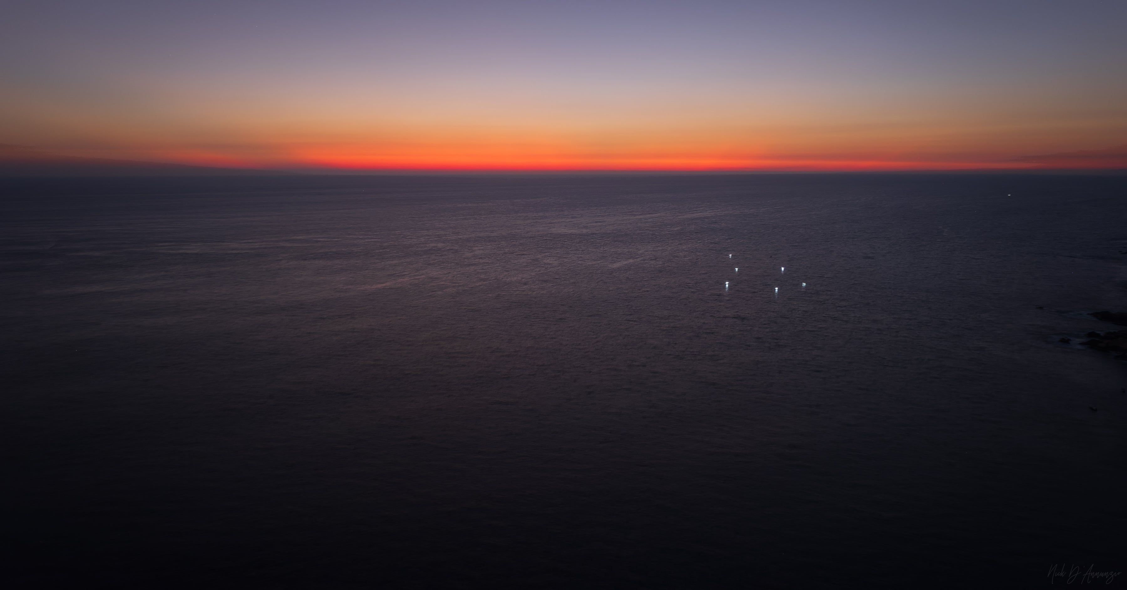 Sunset over a body of water with a dark sky transitioning from orange to blue.
