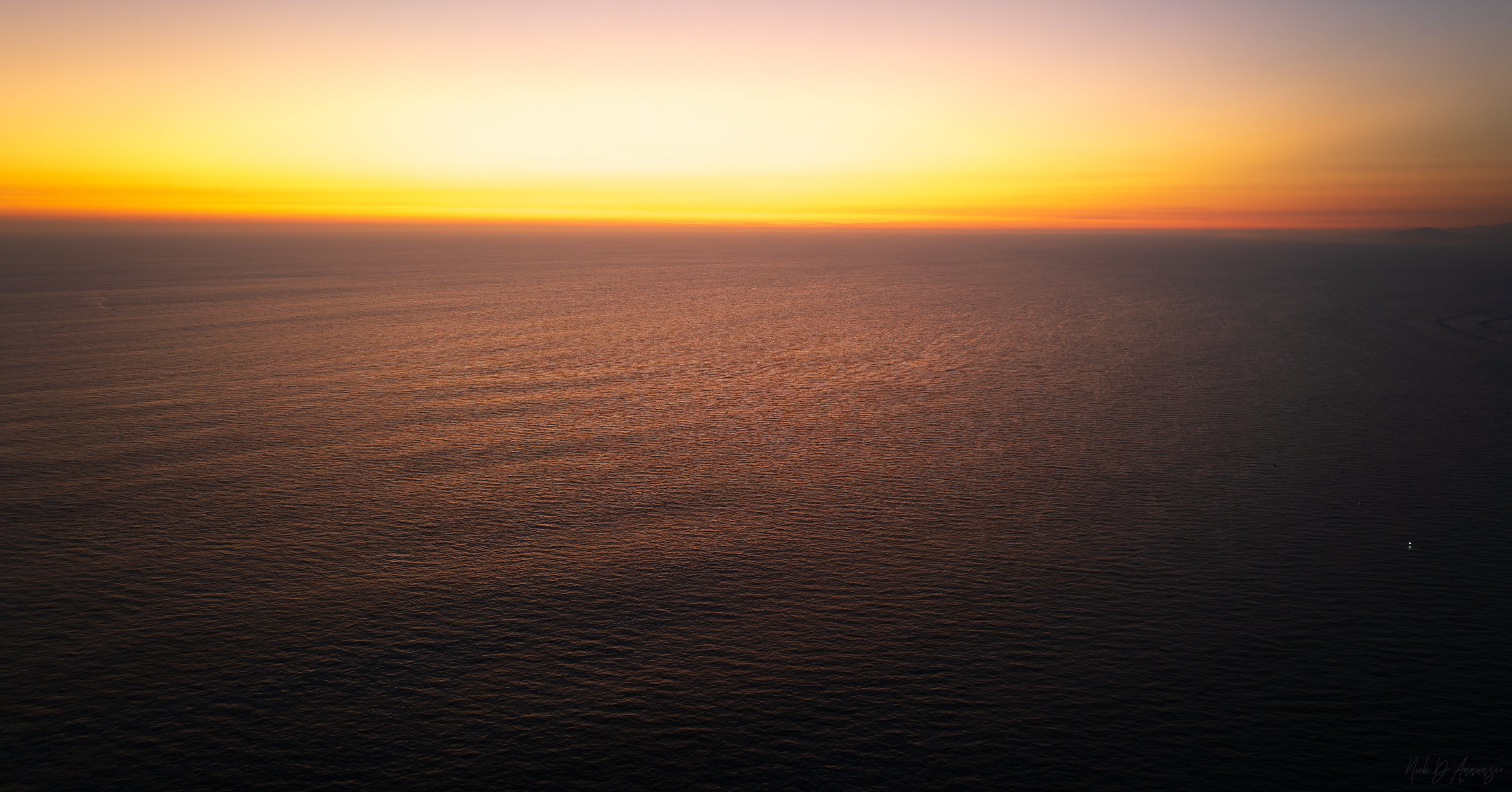 Sunset over a calm ocean with a warm orange sky.