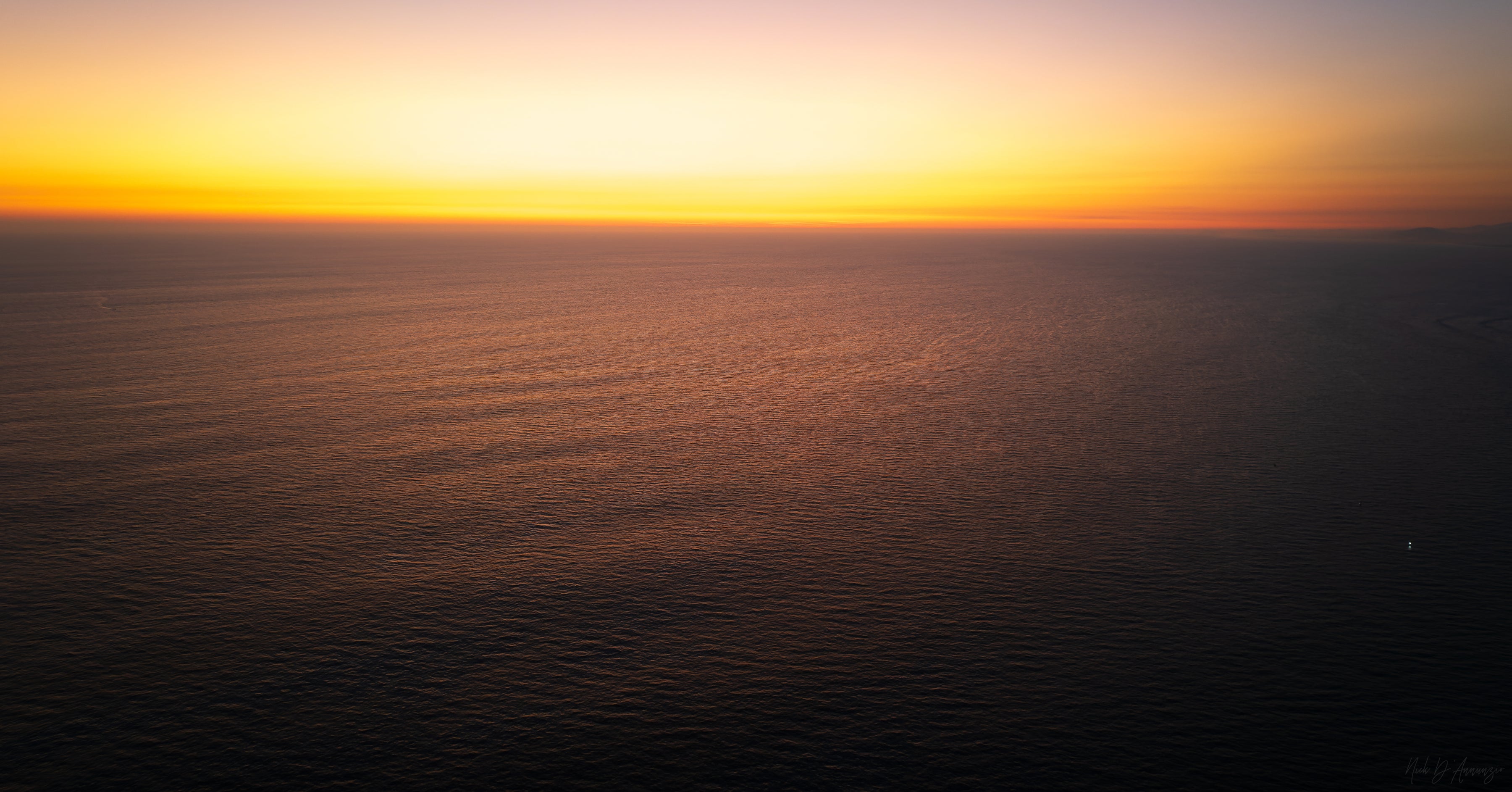 Sunset over a calm ocean with a warm orange sky.