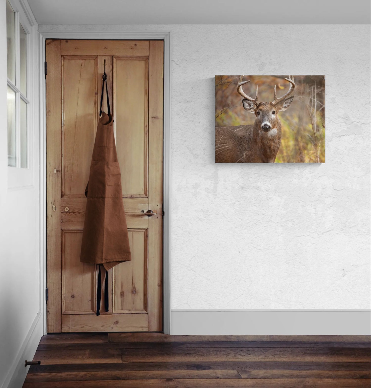 Wooden door with a brown apron hanging on it, next to a wall with a deer print.
