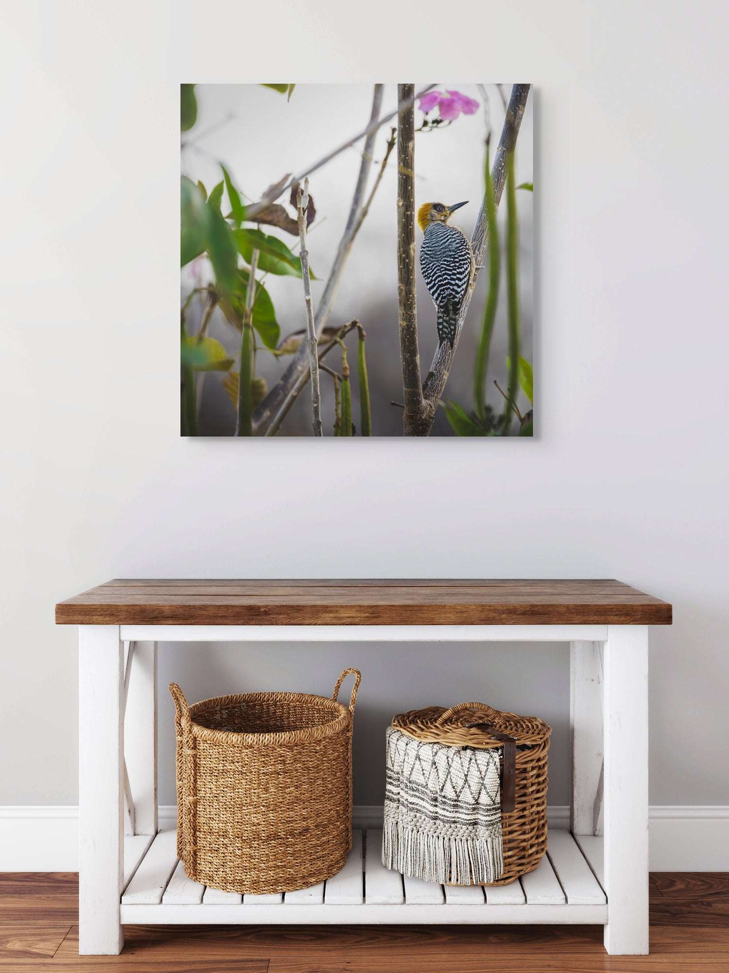 Wooden bench with two baskets underneath, featuring a bird painting above on a white wall.