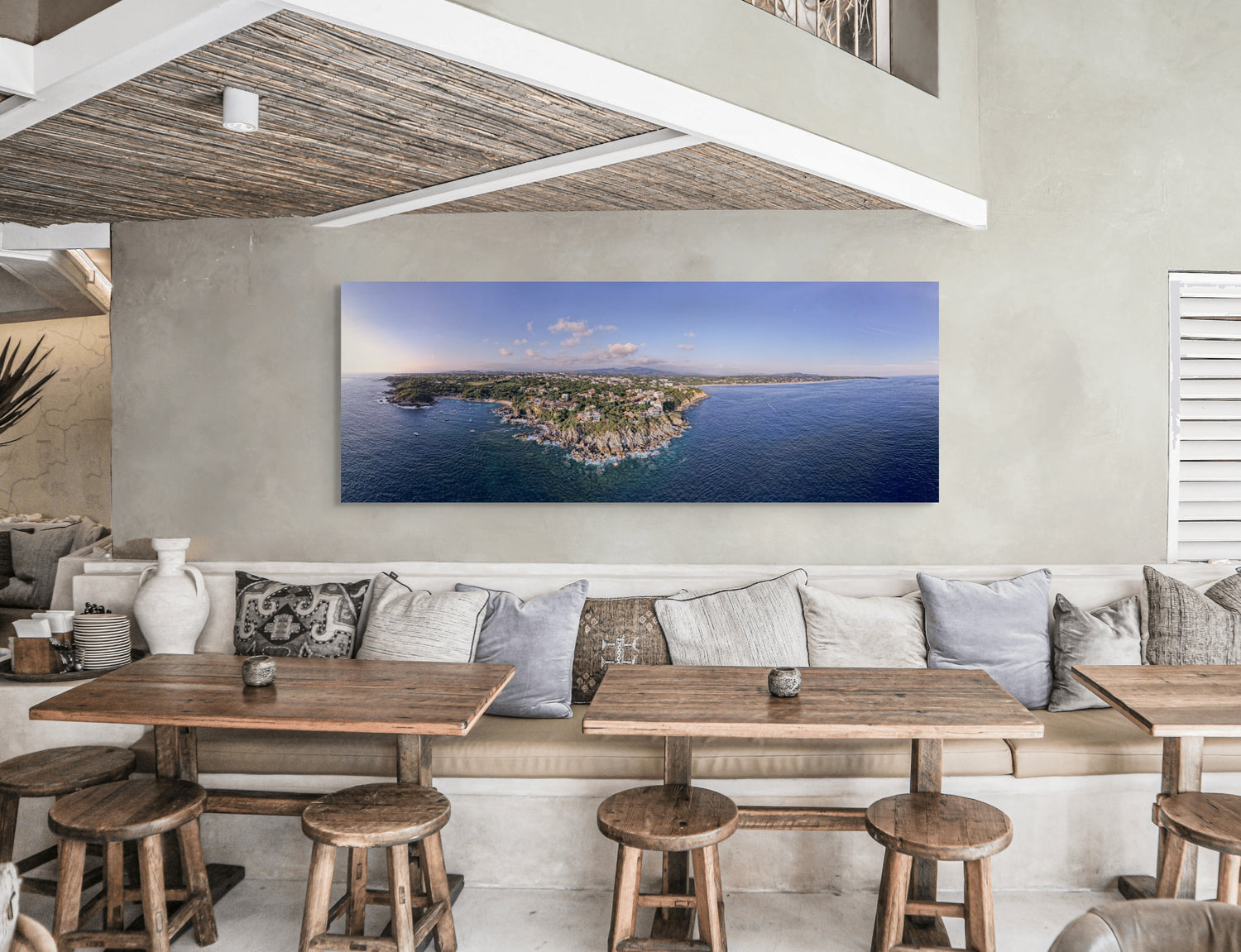 Modern interior with wooden tables, stools, and a large wall-mounted canvas of a coastal scene.